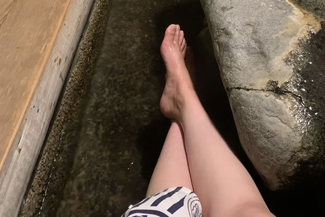 温泉街の足湯でくつろぐ様子。浴衣姿で気軽に楽しめる足湯に足を浸してリラックスしている