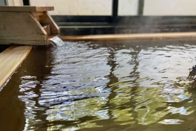 木製の湯口から温泉が注がれる露天風呂の湯面