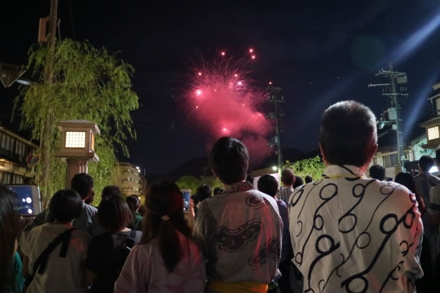 Spectators in yukata looking up at the Natsu Monogatari (Summer Story) Yume Hanabi fireworks lighting up the night sky of Kinosaki Onsen