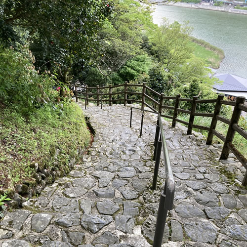 A well-maintained cobblestone staircase with a handrail on the Genbudo Park trail, overlooking a river.
