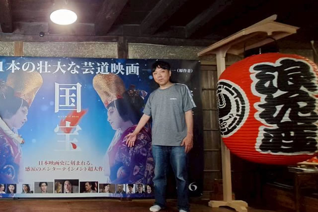Hiroshi Akiyama standing next to the 'National Treasure' movie poster and a large lantern at Eirakukan Theater.